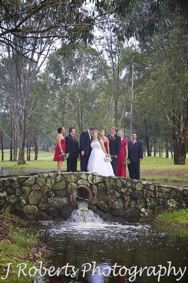 Bride and groom kissing with bridal party laughing - wedding photography sydney